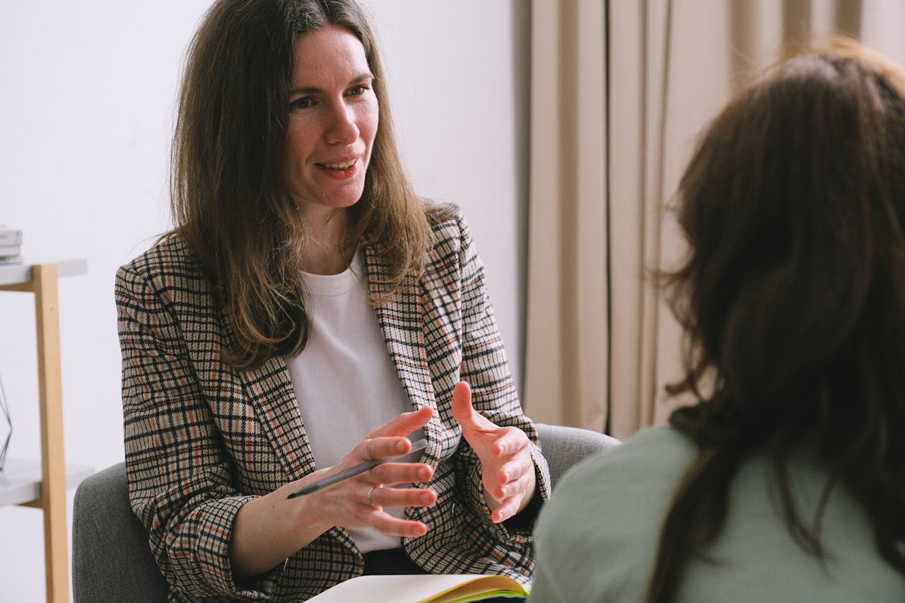 Services-03 Pensive woman psychologist with brown hair in stylish clothes sitting and talking with unrecognizable female in light room